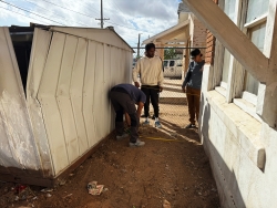 Three people holding a measuring tape on the side of a house.