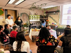 A group of people sitting and watching one person behind a white table demonstrating something.