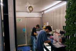 Two people standing next to each other, bent down writing on plastic ziplock bags.