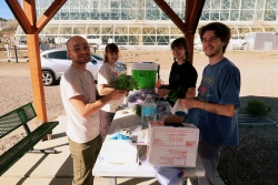 A group of people standing and smiling at a table that is underneath a ramada. They are each holding plants and napkins. 