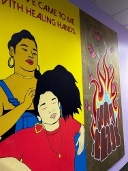 A wall mural where two people are painted. One person is doing the other persons hair. The painting next to them is of wooden logs on fire.