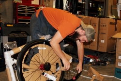 A person fixing a bike while leaning over a bike wheel.