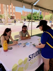 A person talking to two other people who are sitting behind a table covered in white cloth.