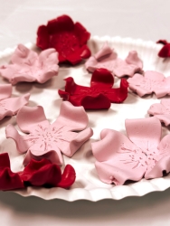 A plate that is filled with clay cherry blossoms. Some are made with light pink clay and others with dark pink clay.