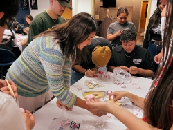 A group of people sitting down at a table making clay cherry blossoms.