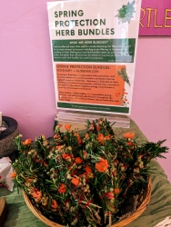 Multiple spring-protection herb bundles on a circular basket. A sign is shown behind the herbs.