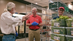 President Robbins talks with two people from Biosphere with plastic and clear tubs filled with baby lettuce inside the Campus Pantry. 
