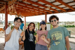 four people smiling together, holding carrots they just picked