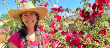 A woman stands in front of several hollihock plants