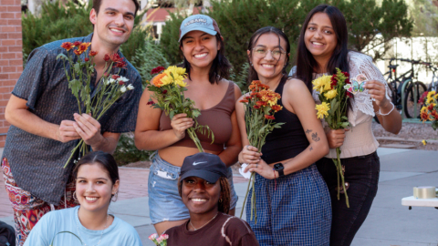 Five students pose together, each holding a bouquet of flowers
