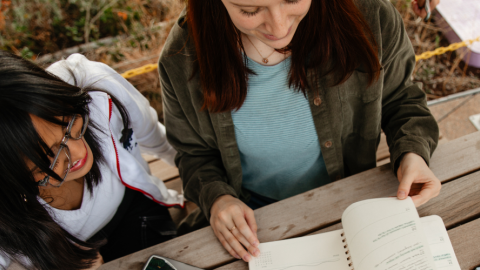 Two women sitting together looking over notes in a notebook