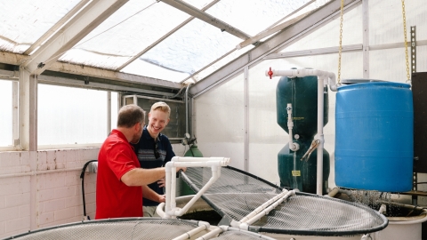 2 people standing next to hydroponic fixtures. 