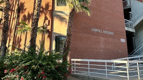 Photo of outside of the Harvill building, showing the building's name on the brick with palm trees out front.