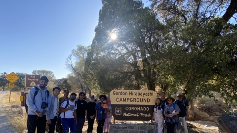 Group of students gathered around the Gordon Hirabayashi Campground sign at Babad Do'ag