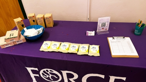 A table covered in a purple cloth with the FORCE logo. On top of the table are various boxes of menstrual cups and wipes. 