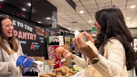 A person holding a reusable tote bag and grabbing produce from another person.