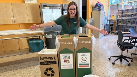 an employee poses with Outdoor Rec's composting and TerraCycle bins, demonstrating how the team is encouraging minimizing their waste!