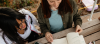 Two women sitting together looking over notes in a notebook